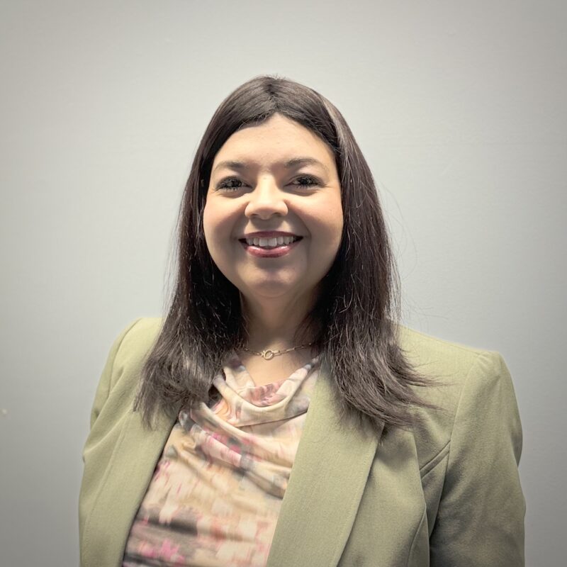 a woman smiles, with long dark hair and wearing a light green suit jacket.