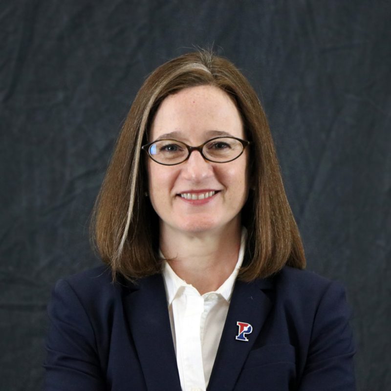 Photo of Kathleen Shields Anderson, she has shoulder-length brown hair, oval-shaped glasses, and is wearing a blue blazer with a white shirt.