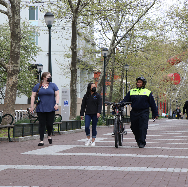 Two Penn students walking on Locust Walk with a security officer who is holding her bike.
